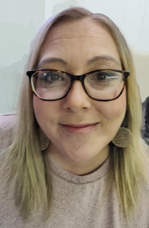 Woman smiling with glasses, wearing earrings.